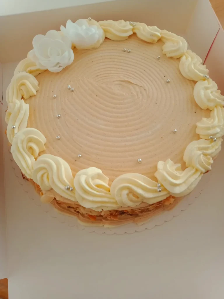 Gâteau rond décoré de crème vanille, fleurs blanches et perles argentées